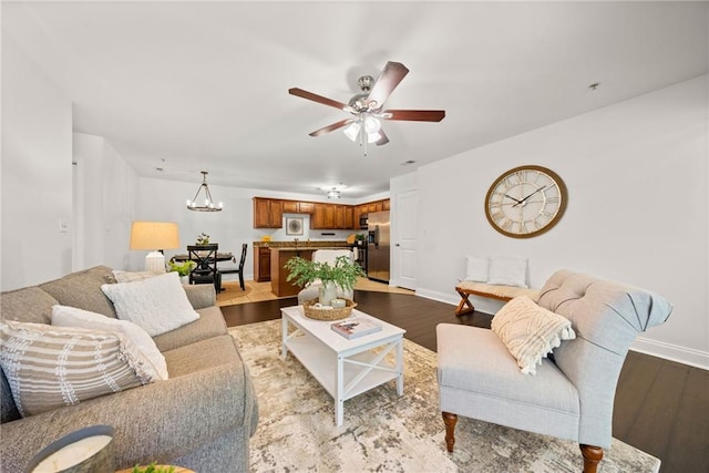 living area featuring ceiling fan with notable chandelier, baseboards, and wood finished floors