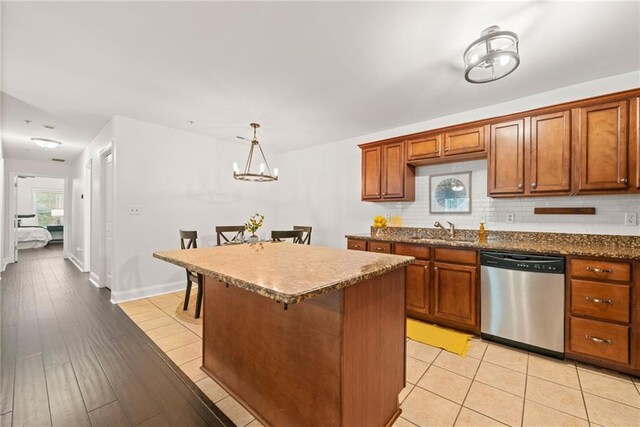 kitchen featuring brown cabinets, a sink, stainless steel dishwasher, tasteful backsplash, and a center island