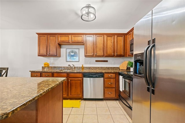 kitchen featuring light tile patterned floors, brown cabinets, a sink, appliances with stainless steel finishes, and tasteful backsplash