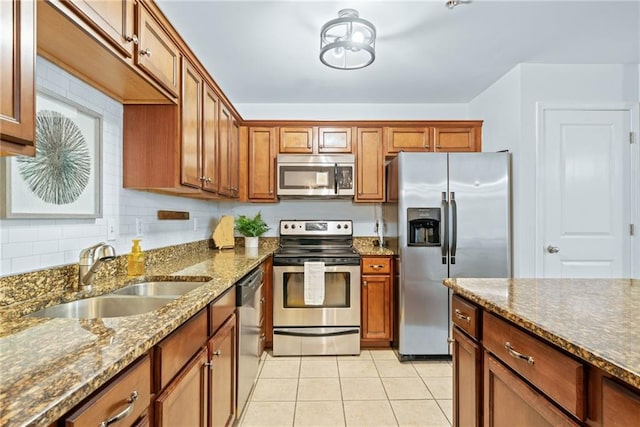 kitchen with tasteful backsplash, light tile patterned floors, brown cabinets, stainless steel appliances, and a sink