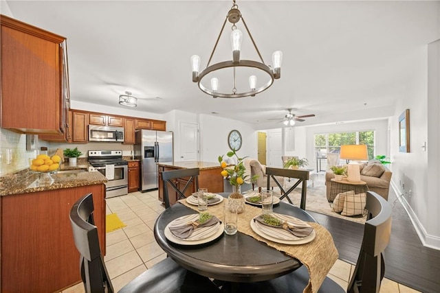 dining space with light tile patterned flooring, ceiling fan with notable chandelier, and baseboards