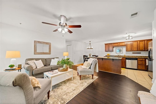 living area featuring ceiling fan with notable chandelier, visible vents, and light wood-type flooring