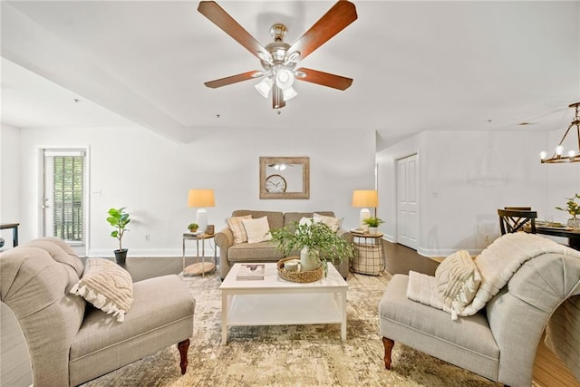 living area with ceiling fan with notable chandelier, wood finished floors, and baseboards