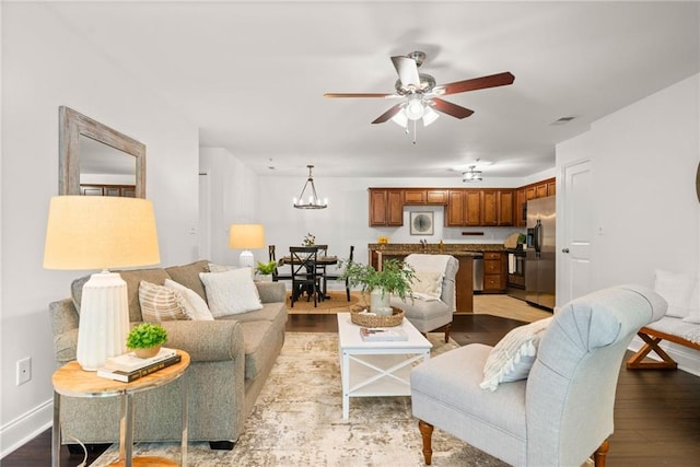 living area with visible vents, light wood-style flooring, ceiling fan with notable chandelier, and baseboards