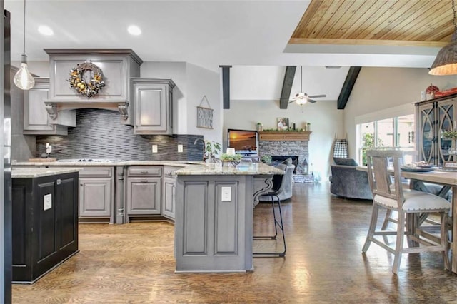 kitchen featuring gray cabinets, a kitchen breakfast bar, a ceiling fan, tasteful backsplash, and a peninsula