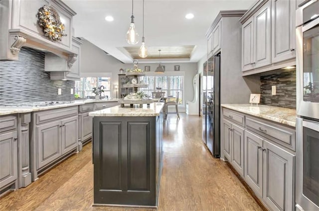 kitchen with gray cabinetry, decorative backsplash, stainless steel appliances, and light wood-type flooring