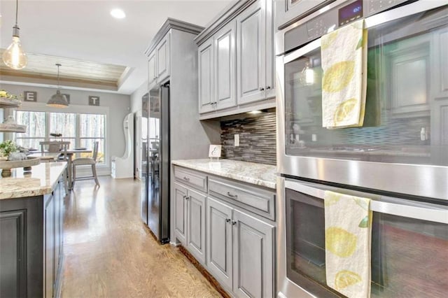 kitchen featuring a raised ceiling, double oven, light wood-style flooring, backsplash, and gray cabinetry