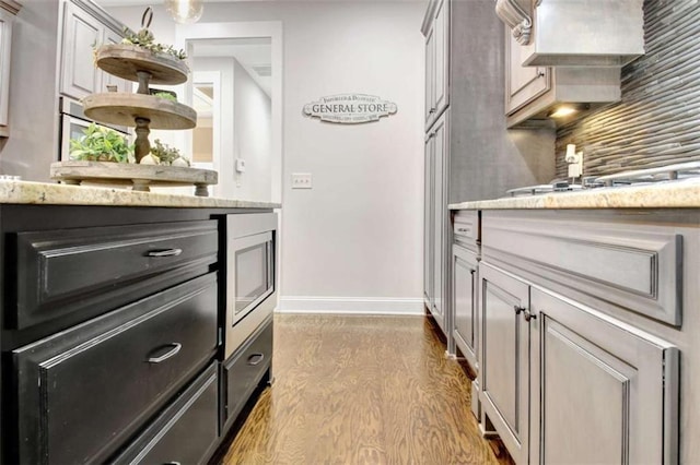 interior space featuring wood finished floors, baseboards, stainless steel microwave, light stone counters, and backsplash
