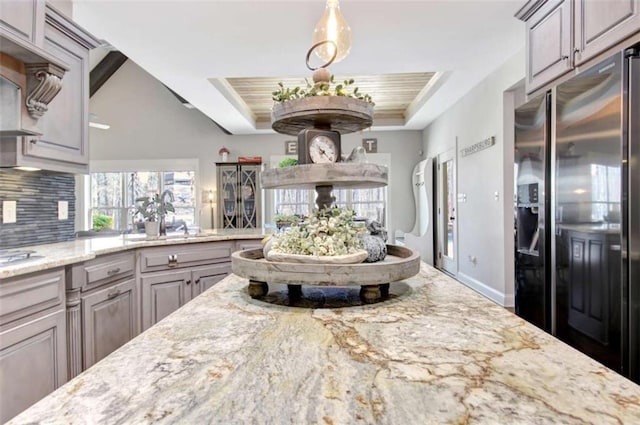 kitchen featuring tasteful backsplash, light stone countertops, a sink, a raised ceiling, and stainless steel appliances