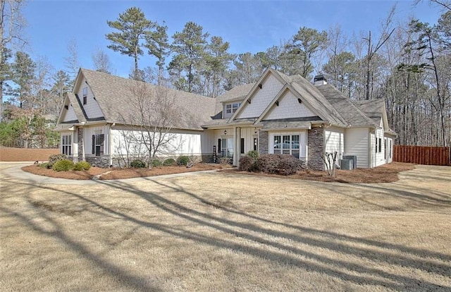 view of front facade with driveway, a chimney, central AC, fence, and stone siding