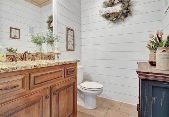 bathroom with vanity, tile patterned floors, wooden walls, and toilet