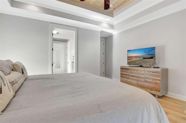 bedroom with baseboards, ornamental molding, wood finished floors, and a tray ceiling