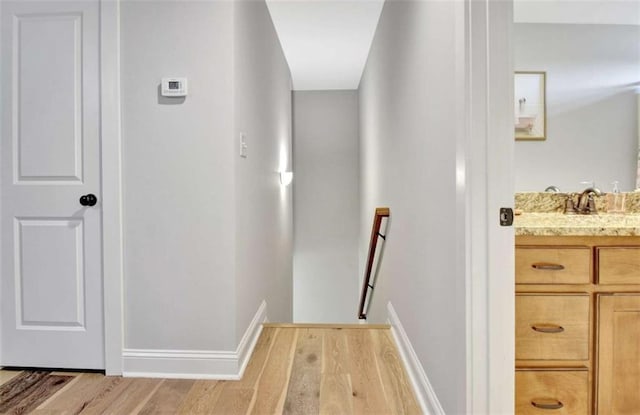 corridor with light wood-style floors, baseboards, a sink, and an upstairs landing