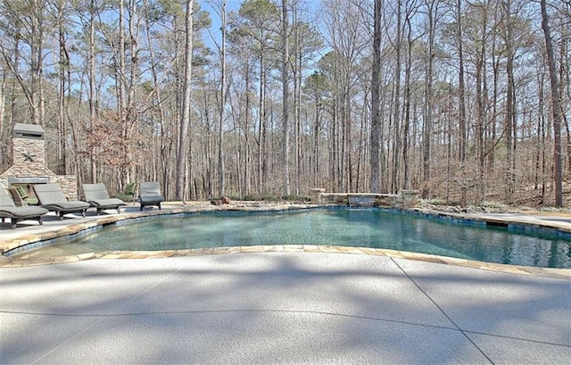 view of swimming pool with a patio, a swimming pool, and a forest view