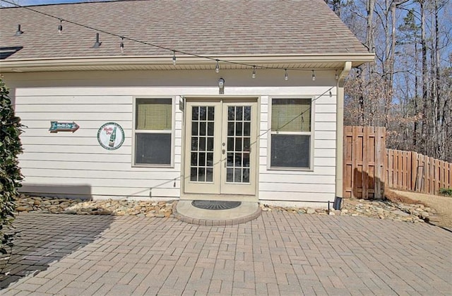 entrance to property featuring a patio area, roof with shingles, fence, and french doors