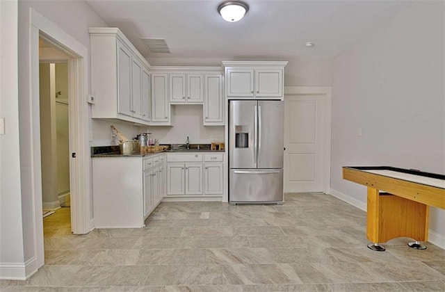 kitchen featuring stainless steel refrigerator with ice dispenser, visible vents, dark countertops, baseboards, and white cabinets
