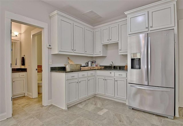 kitchen featuring visible vents, a sink, stainless steel fridge with ice dispenser, dark stone countertops, and white cabinetry
