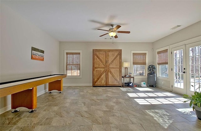 game room with baseboards, a ceiling fan, stone finish floor, and a wealth of natural light