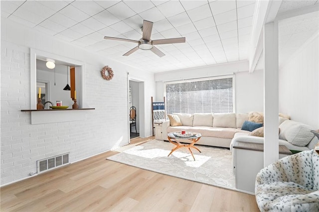 living room with visible vents, ceiling fan, brick wall, and wood finished floors