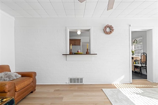 living room featuring ornamental molding, visible vents, brick wall, and wood finished floors