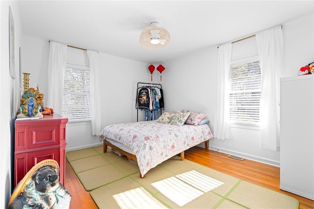 bedroom with baseboards, visible vents, and wood finished floors