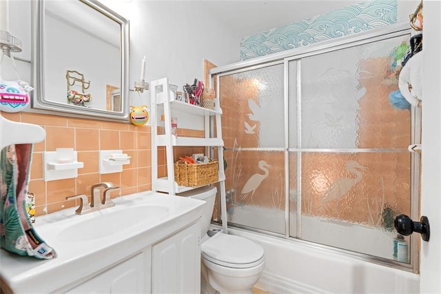 full bathroom featuring toilet, bath / shower combo with glass door, tile walls, and vanity