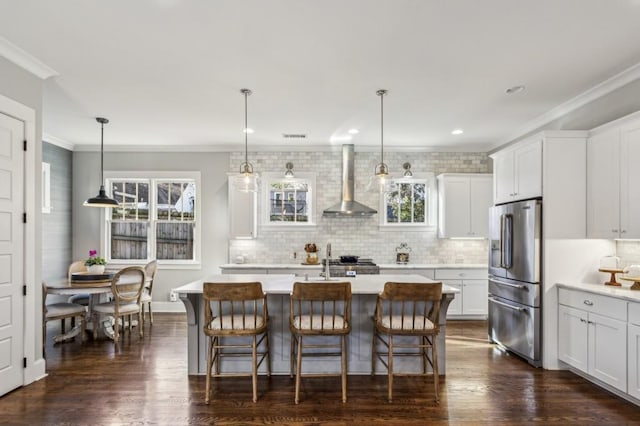 kitchen featuring crown molding, light countertops, high end refrigerator, and wall chimney range hood