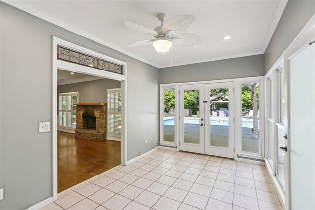 doorway with french doors, baseboards, a stone fireplace, light tile patterned flooring, and crown molding
