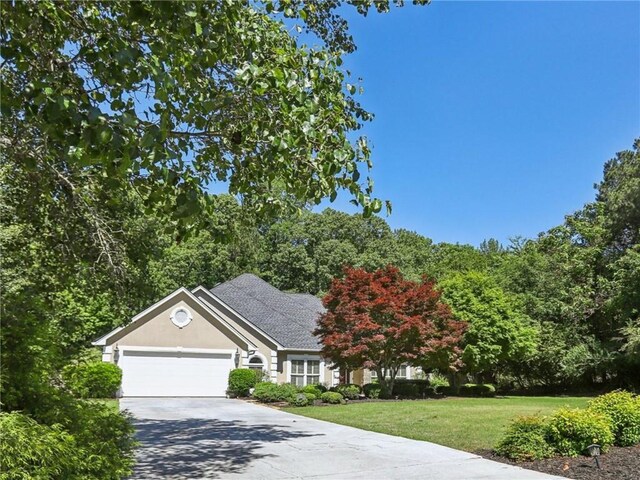 view of property hidden behind natural elements featuring a front lawn, a garage, driveway, and stucco siding