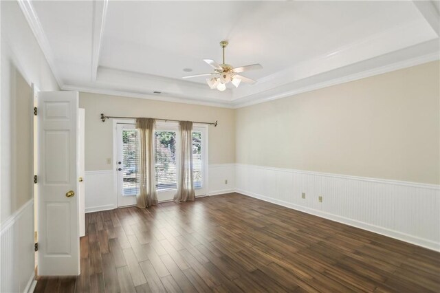 unfurnished room with a raised ceiling, a wainscoted wall, ceiling fan, dark wood-type flooring, and crown molding