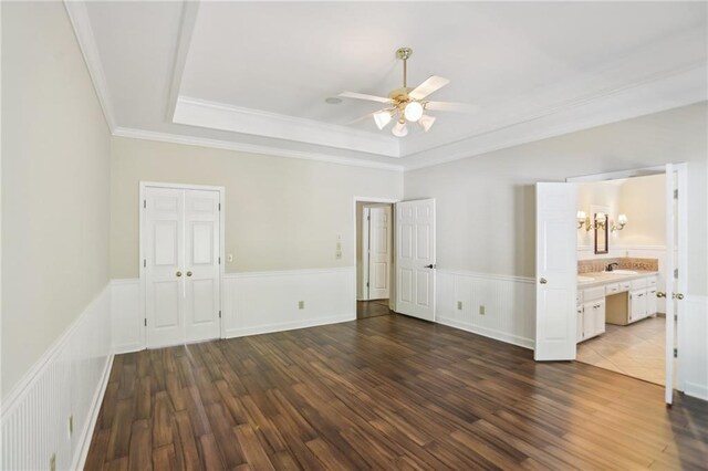 unfurnished room featuring a tray ceiling, ceiling fan, dark wood-type flooring, ornamental molding, and a wainscoted wall