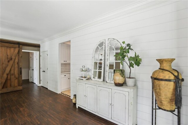 hall with a barn door, dark wood-type flooring, and ornamental molding