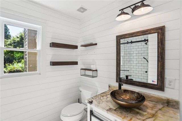 bathroom with vanity, toilet, a tile shower, and wood walls