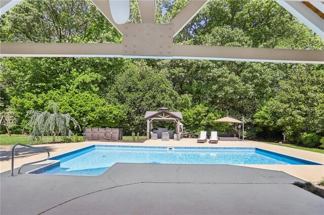 swimming pool with a gazebo, a patio area, and view of scattered trees