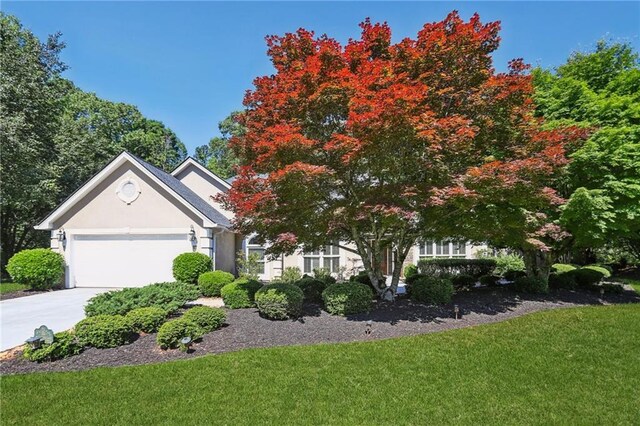 view of front facade with an attached garage, a front yard, concrete driveway, and stucco siding
