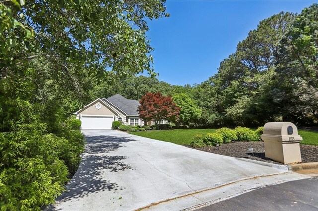 view of property hidden behind natural elements featuring driveway, a garage, and a front lawn