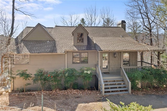 view of front facade featuring covered porch, a chimney, and a shingled roof