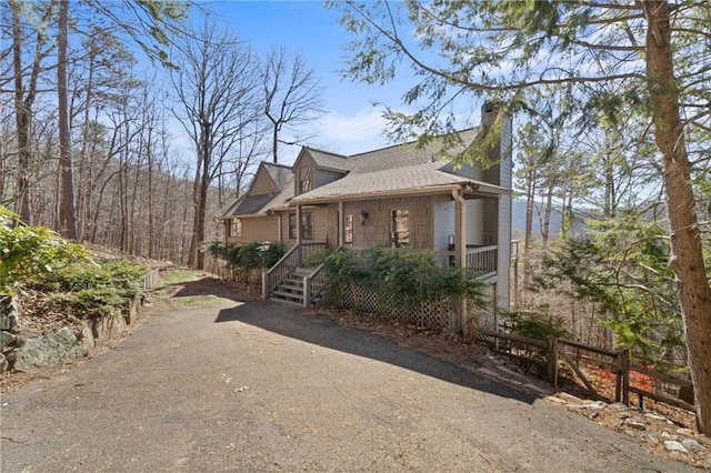 view of front of home featuring aphalt driveway, a porch, a chimney, and fence