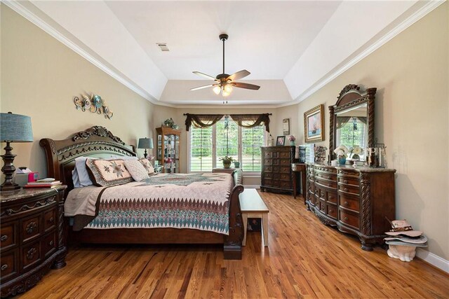 bedroom featuring ceiling fan, light wood-type flooring, a raised ceiling, and multiple windows