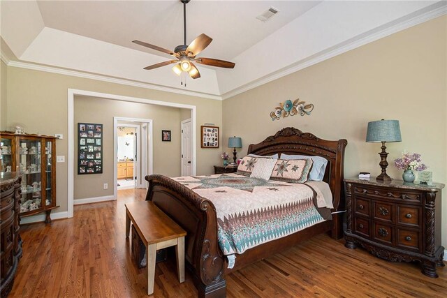 bedroom with wood-type flooring, a tray ceiling, ceiling fan, ornamental molding, and ensuite bath