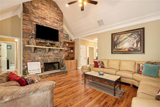 living room featuring a stone fireplace, ceiling fan, hardwood / wood-style flooring, and crown molding