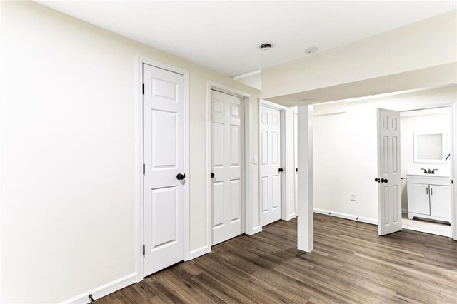 unfurnished bedroom featuring ensuite bathroom, two closets, dark wood-type flooring, and sink