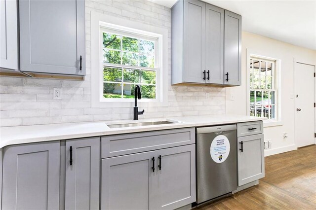 kitchen featuring decorative backsplash, wood-type flooring, gray cabinetry, sink, and dishwasher