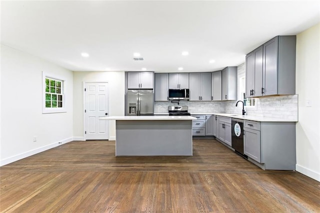 kitchen featuring dark wood-type flooring, appliances with stainless steel finishes, gray cabinetry, and a center island