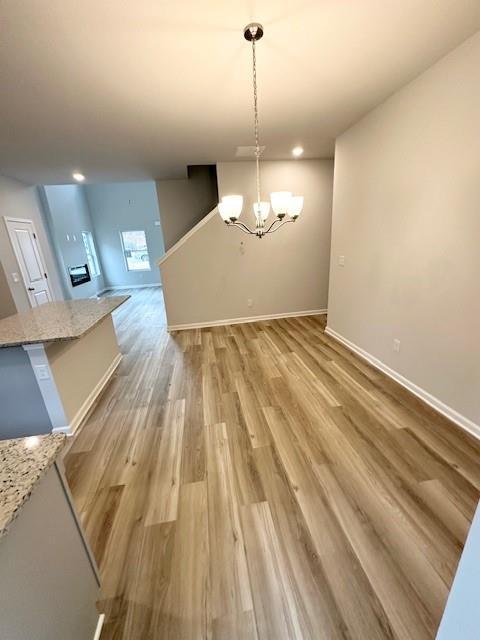 unfurnished dining area featuring a notable chandelier, baseboards, and light wood-style floors