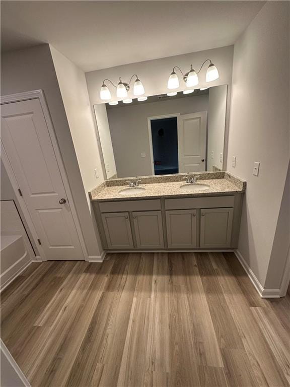 full bathroom featuring double vanity, a sink, baseboards, and wood finished floors