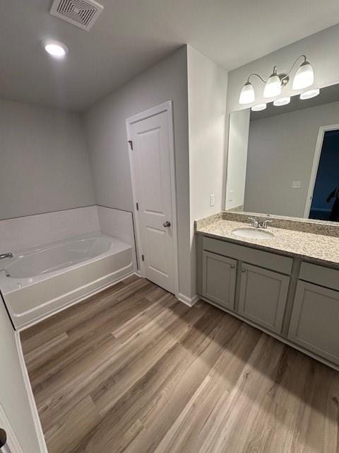 full bath with a garden tub, visible vents, wood finished floors, and vanity