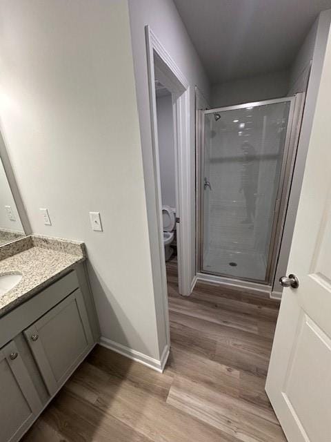 full bath with toilet, wood finished floors, vanity, baseboards, and a shower stall