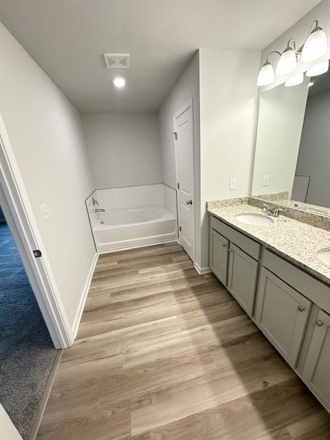 bathroom with wood finished floors, visible vents, a garden tub, and double vanity