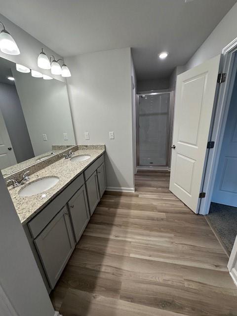 full bathroom featuring double vanity, a stall shower, a sink, and wood finished floors